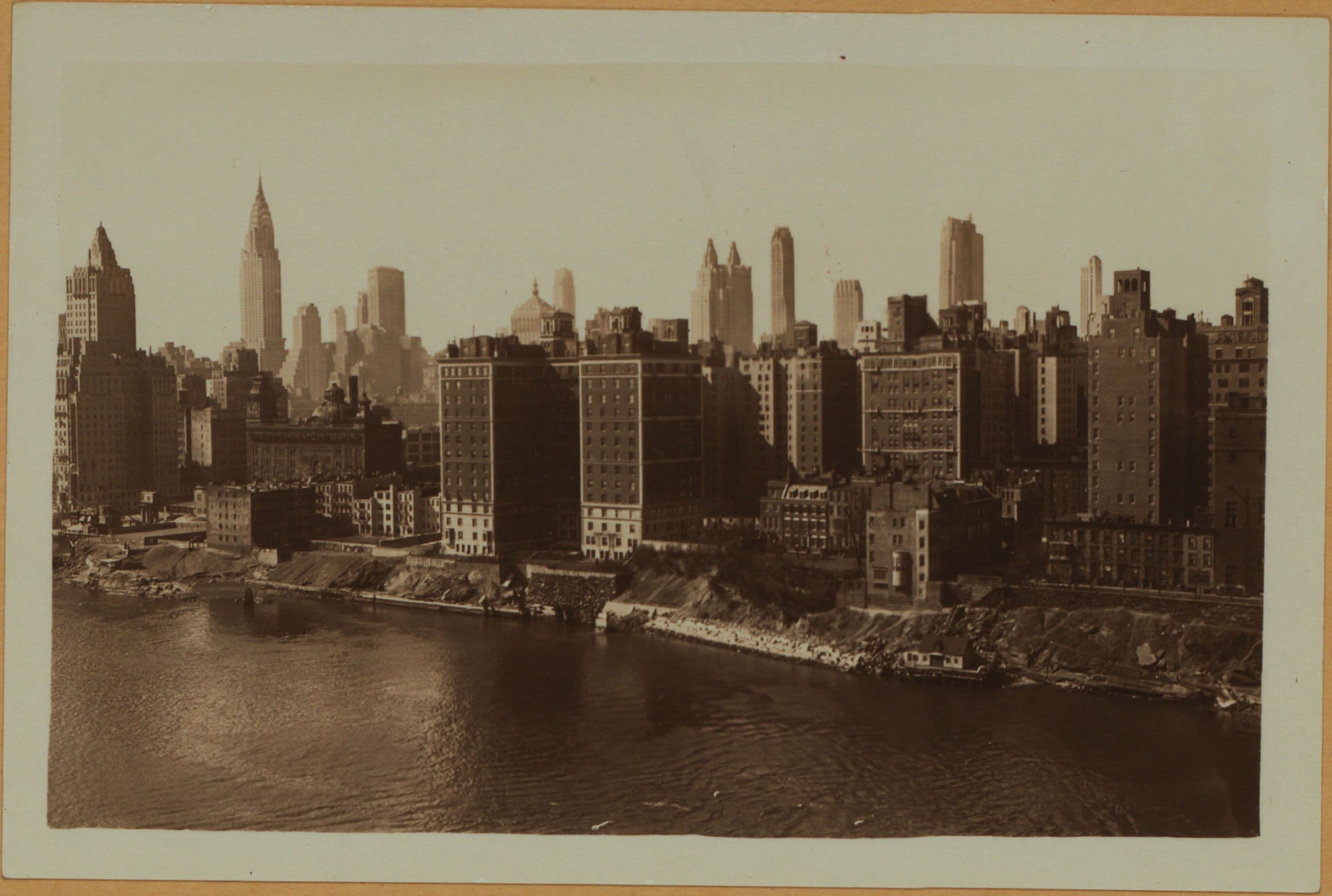 East River - Shore and skyline of Manhattan between East 53rd and 59th Streets - Williamsburg and Queensborough Bridges - [Chrysler Building; General Electric Company; Lincoln Building; New York Central Railroad Building; New York Steam Corporation; R.C.A. Building; River House; Waldorf-Astoria Hotel.]